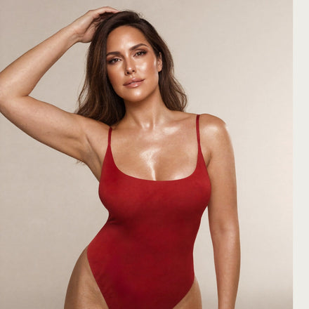 Studio portrait of a woman with bronzed skin in a red swimsuit posing against a neutral background.